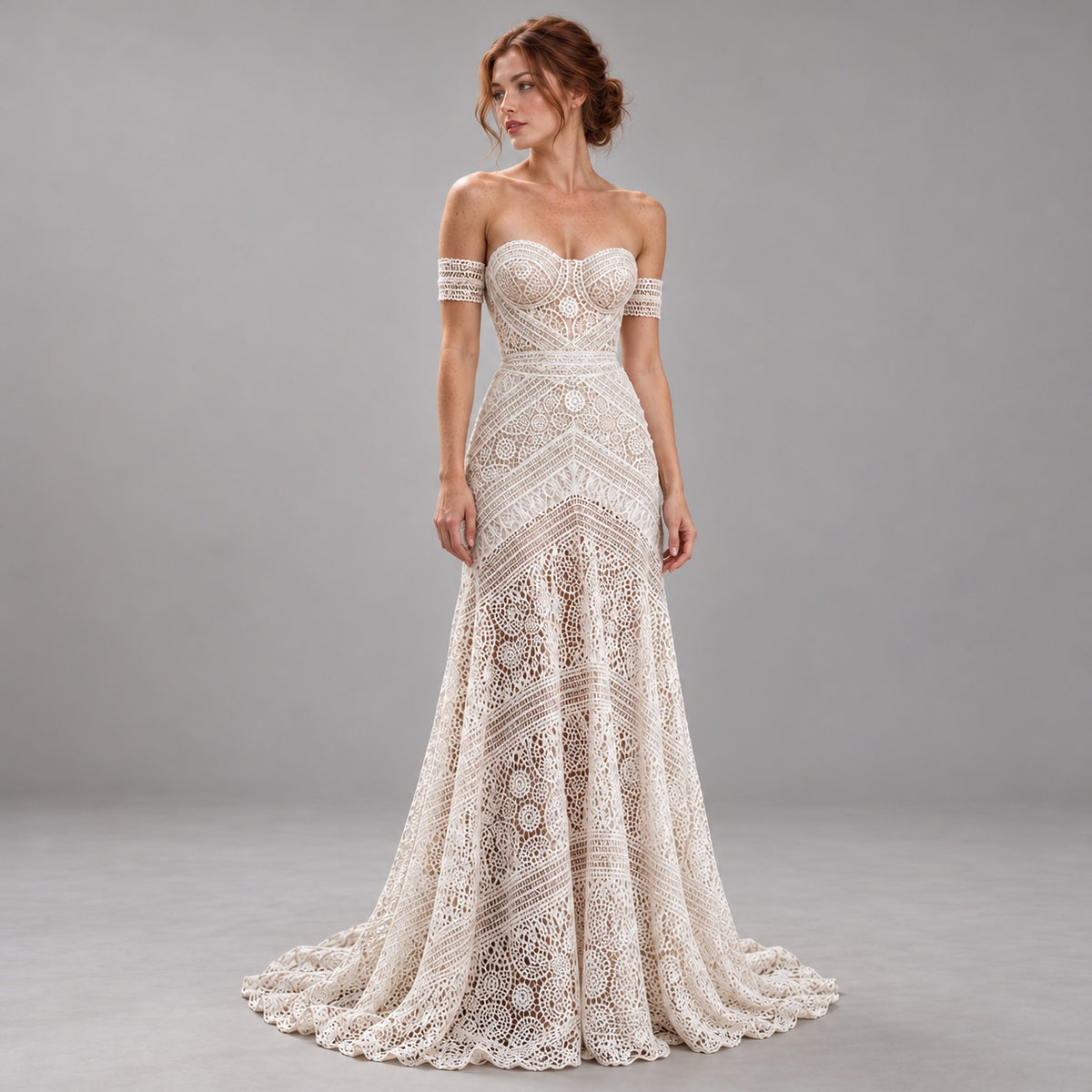An off-the-shoulder lace mermaid gown in a warm ivory or cream tone, featuring intricate geometric and floral lace patterns, worn by a model in a studio setting with a gray background.