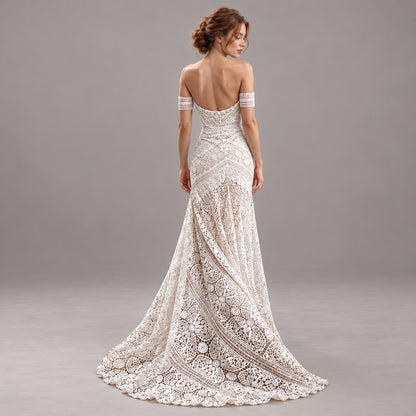 An off-the-shoulder lace wedding gown with a fitted silhouette and dramatic train, shown from the back on a model against a neutral gray studio background.