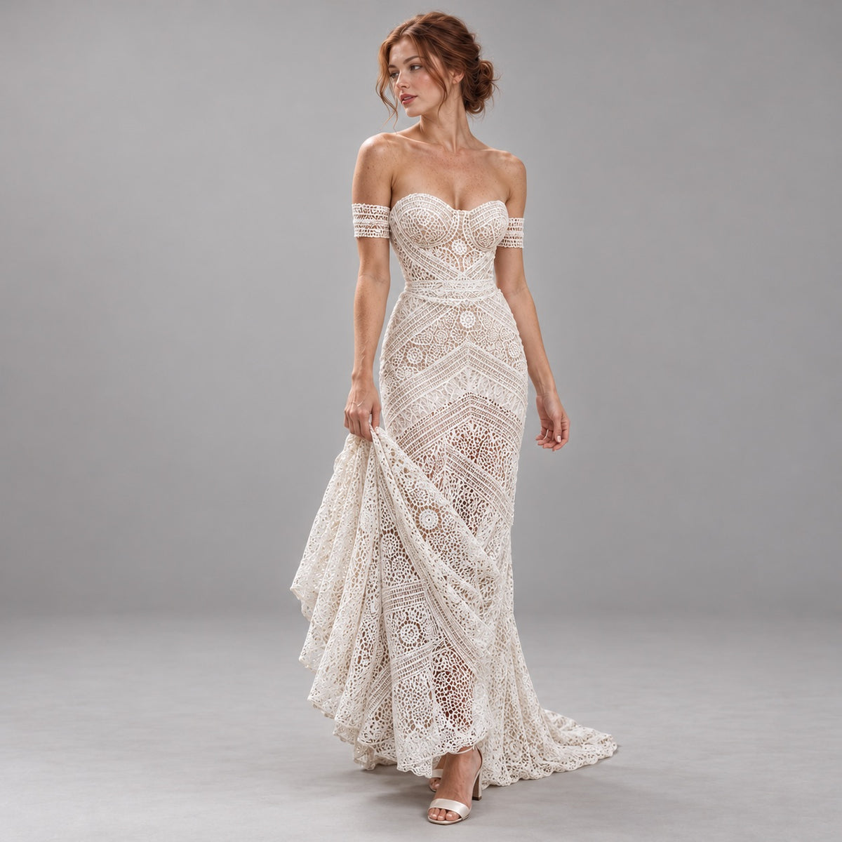 An off-the-shoulder lace wedding gown in an ivory/cream shade, worn by a model in a studio setting with a neutral gray background.
