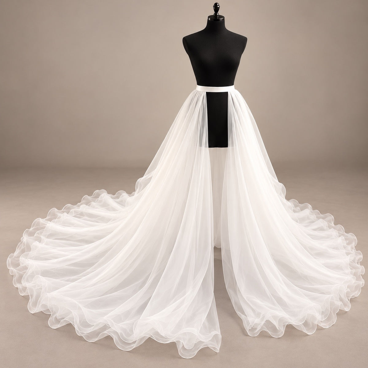 A white organza overskirt or bridal train displayed on a black dress form mannequin against a plain warm beige studio background.