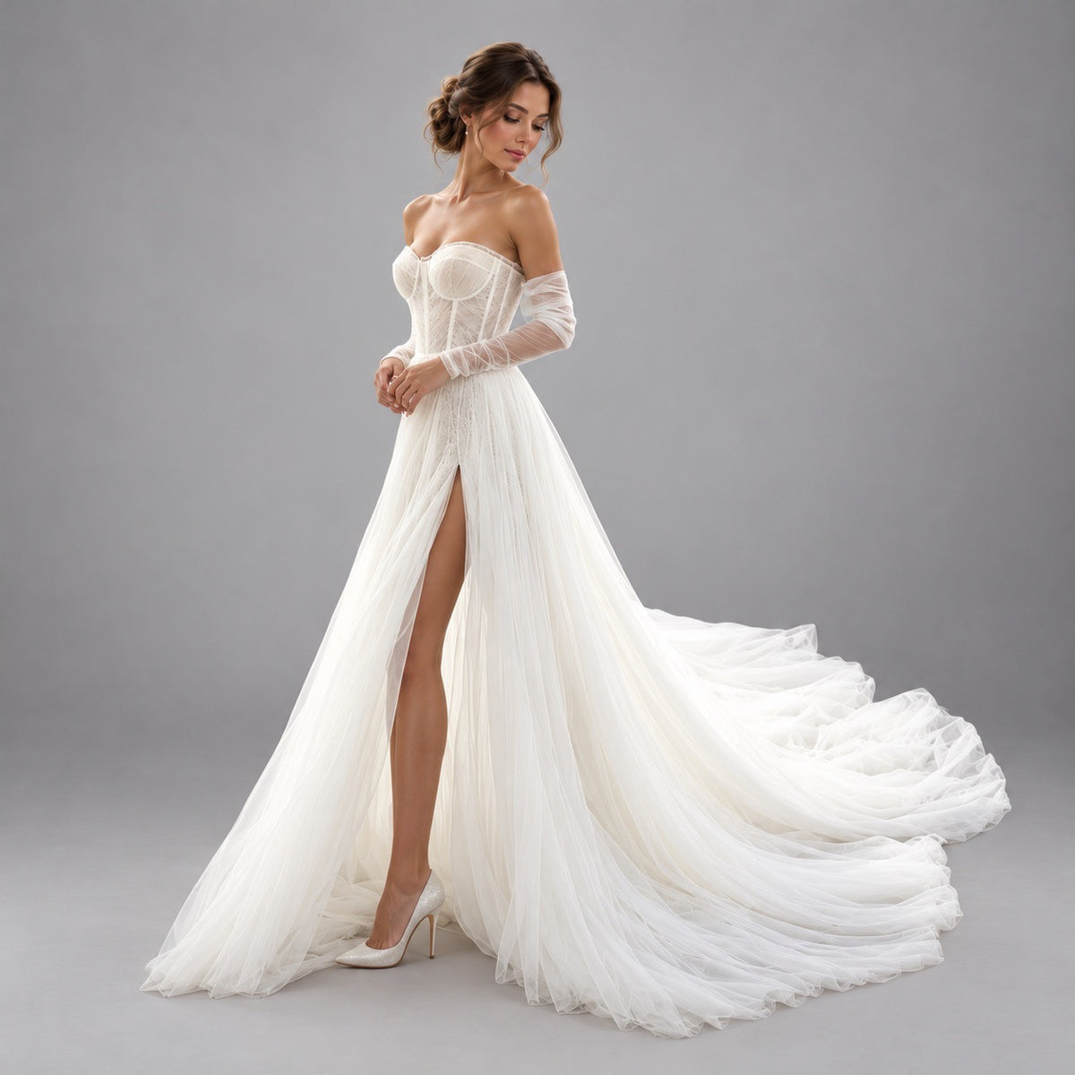 A woman models an off-the-shoulder white wedding gown with a fitted lace corset bodice, sheer long sleeves, a high thigh slit, and a flowing tulle train against a plain gray studio background.