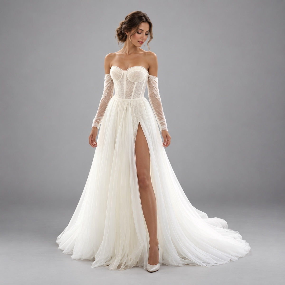 A woman modeling an off-the-shoulder white wedding gown with a lace corset bodice, sheer long sleeves, a high thigh slit, and a flowing tulle skirt with a train, photographed against a plain gray studio background.